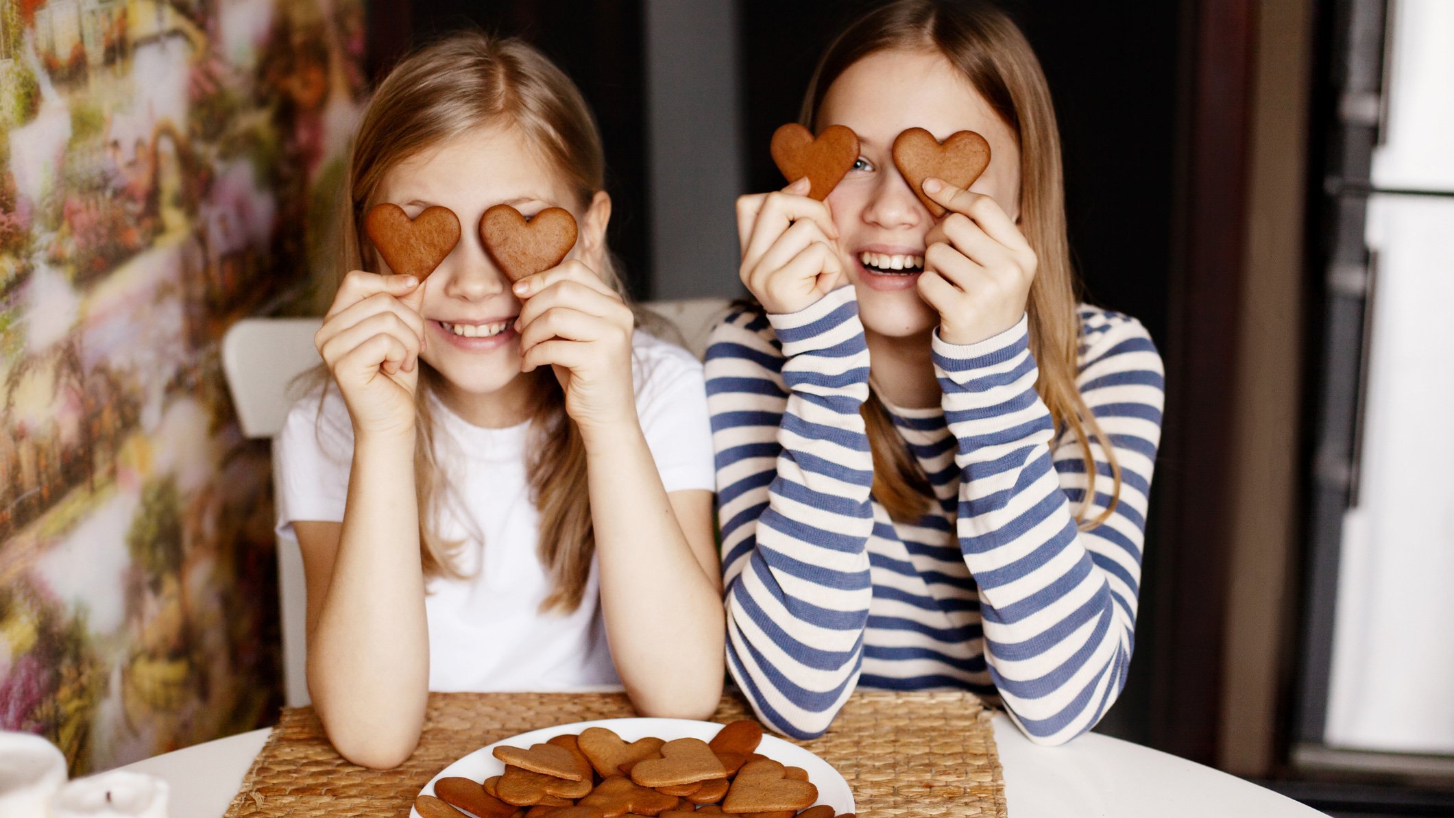 Two girls holding up heart shaped cookies.